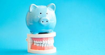 Piggy bank atop model teeth representing cost of cosmetic dentistry in Grafton
