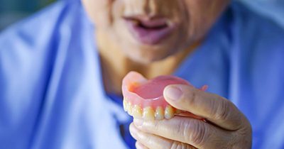 a person with missing teeth holding a denture