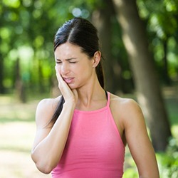 woman in a park holding her cheek in pain 