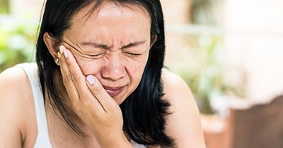 woman in white tank top holding mouth in pain