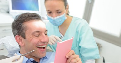 Man in dental chair looking at smile in mirror