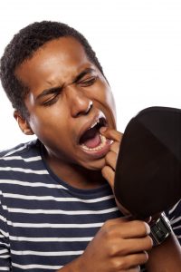 man checking loose tooth in mirror 