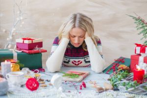 Woman sitting at a holiday table full of gift wrapping supplies grasping her head in frustration