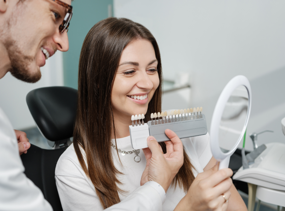 Woman smiling in dental chair while dentist shows her veneer options